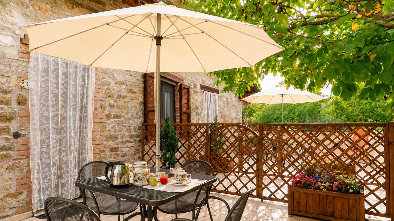 Terrazza accogliente con ombrellone e tavolo apparecchiato, immersa nel verde dell'agriturismo umbro Domus Santa Croce.