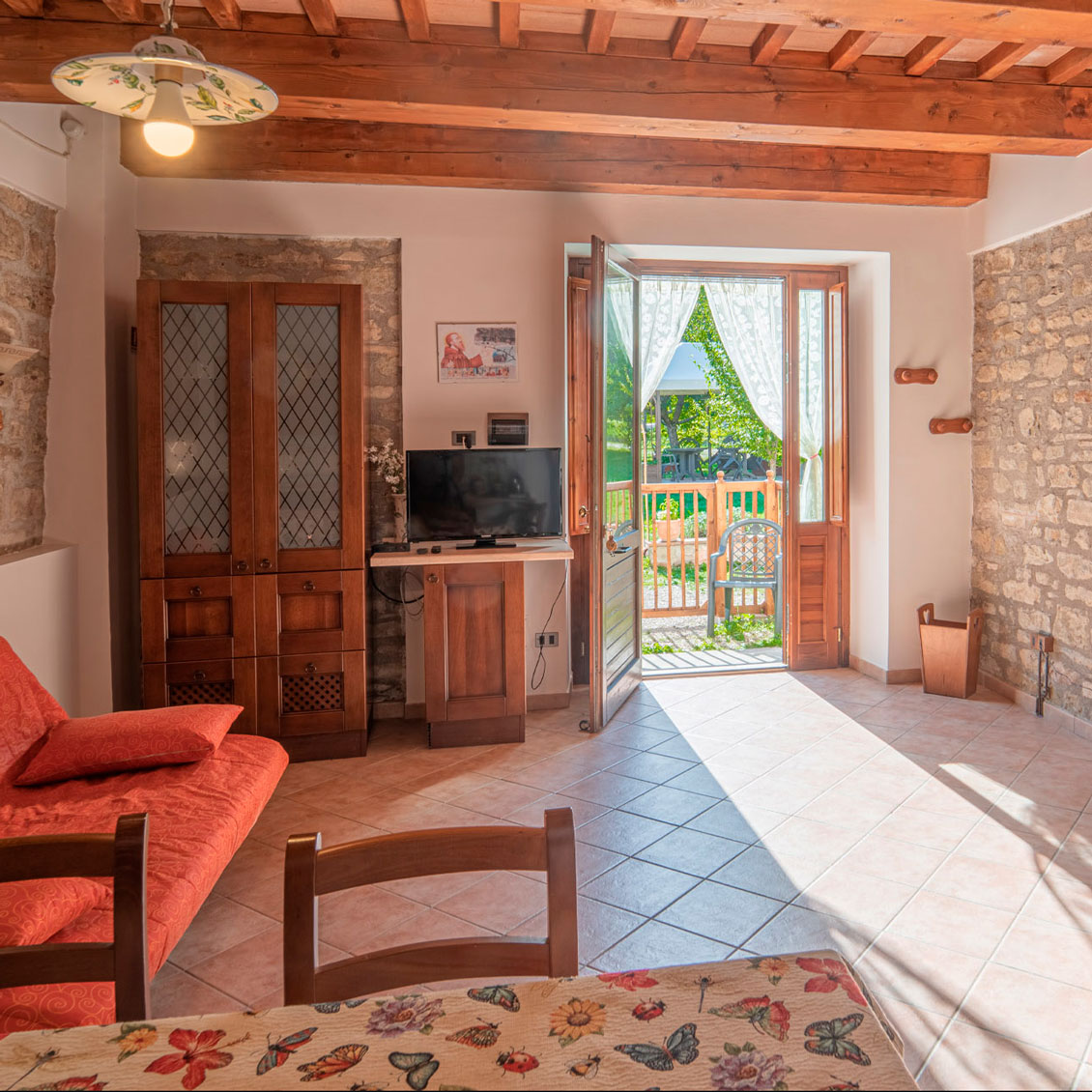 Accogliente soggiorno agriturismo umbro con arredi rustici, luce naturale e vista sul giardino esterno dalla veranda.