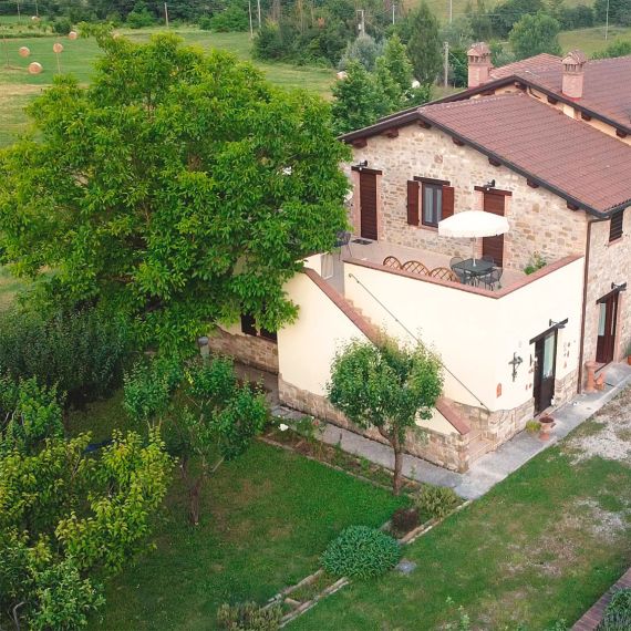 Vista aerea di un agriturismo umbro immerso nel verde: Domus Laetitiae Santa Croce con terrazza accogliente e dettagli in pietra. Perfetto rifugio rurale.