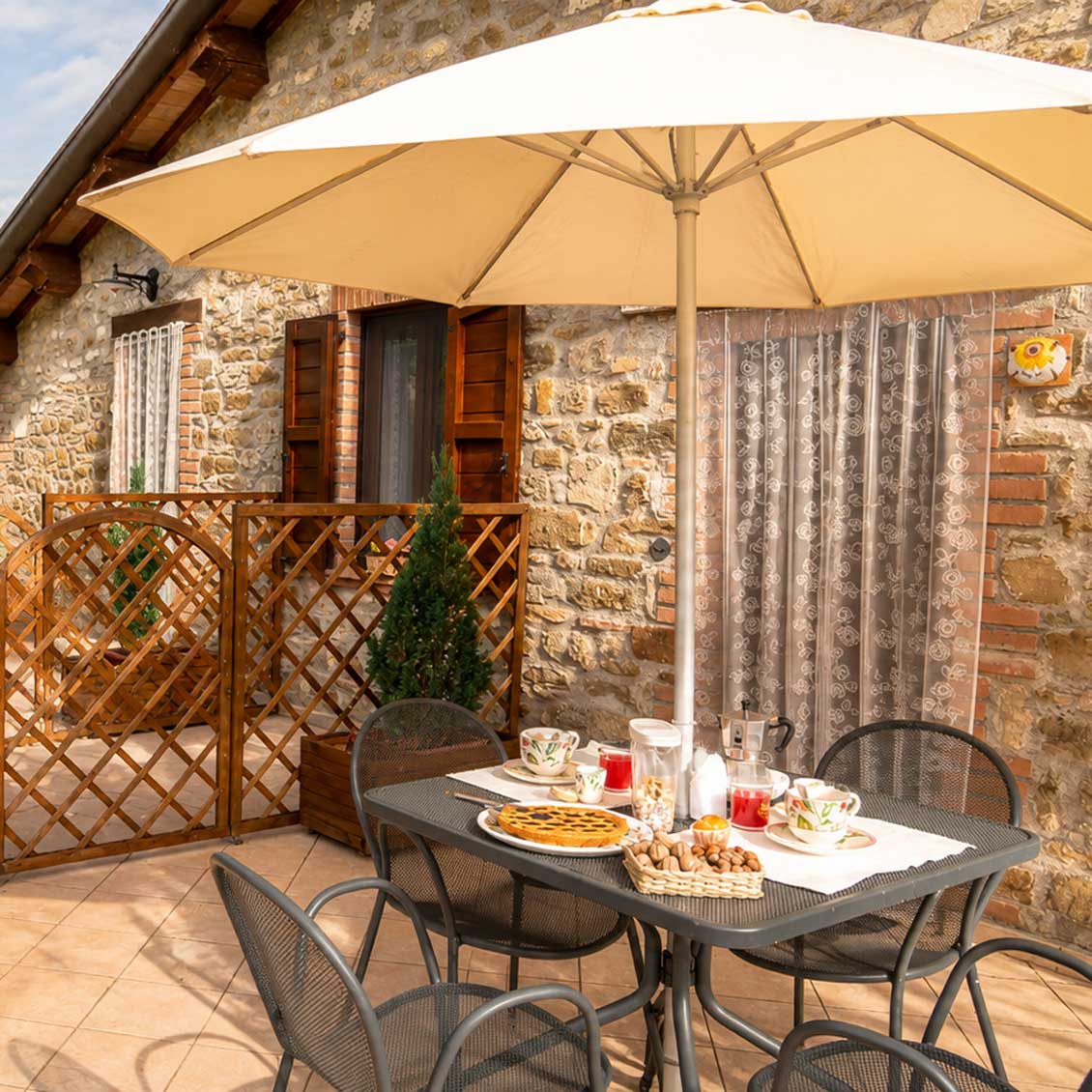 Terrazza rustica umbra con tavolo apparecchiato, ombrellone e sfondo in pietra. Perfetto per colazioni all'aperto.