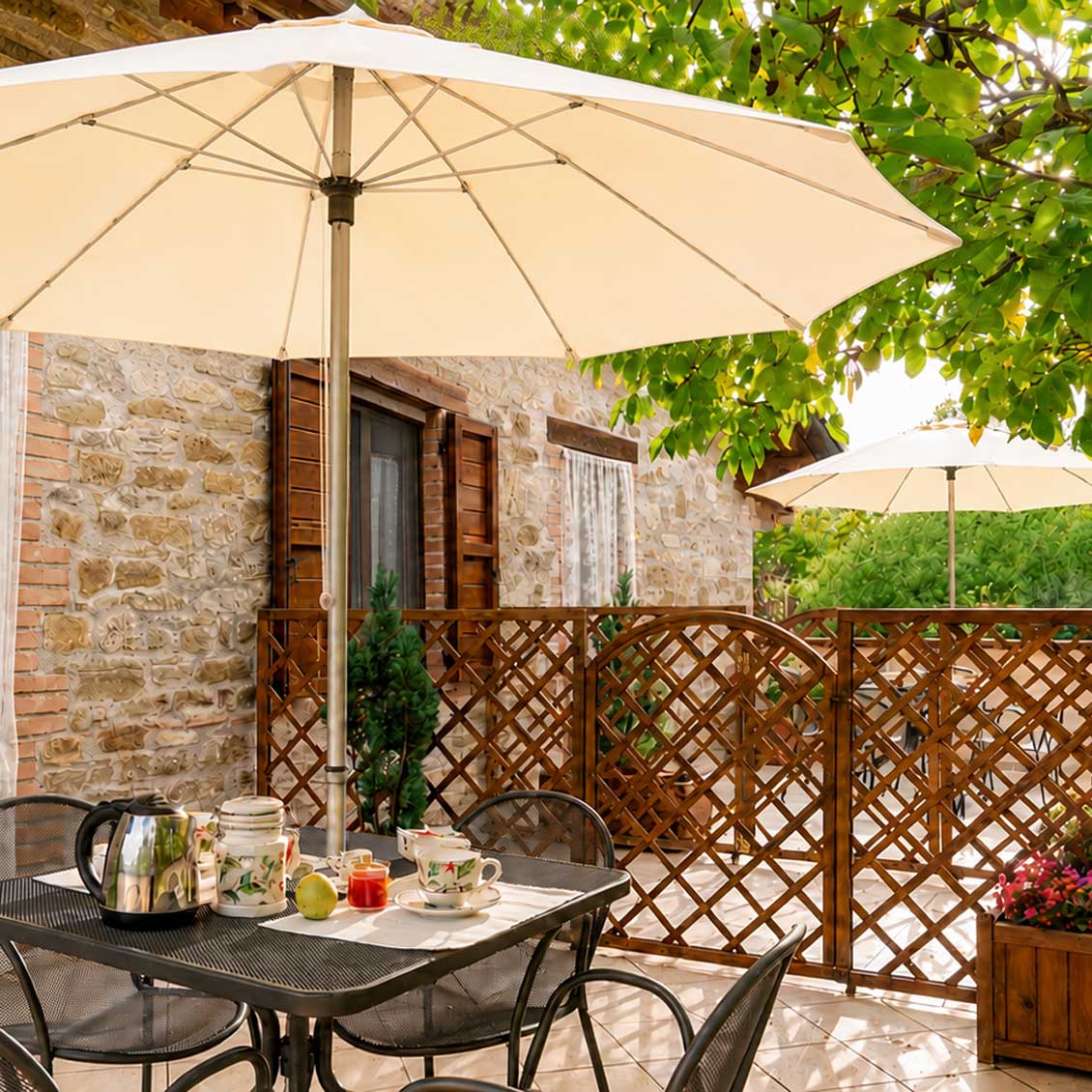 Colazione all'aperto in agriturismo umbro, sotto un ombrellone, con vista su un giardino verde e un casale in pietra.