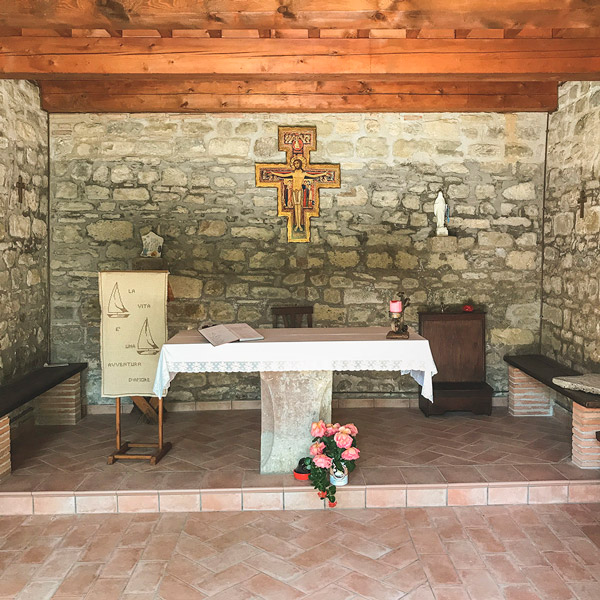 Piccola cappella in pietra nell'agriturismo umbro di Domus Laetitia Santa Croce, atmosfera serena e accogliente con altare decorato e crocefisso.