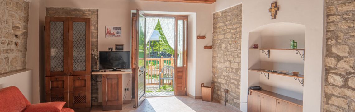 Accogliente soggiorno in agriturismo umbro con porta che si apre su un giardino, ideale per i turisti italiani in cerca di relax.