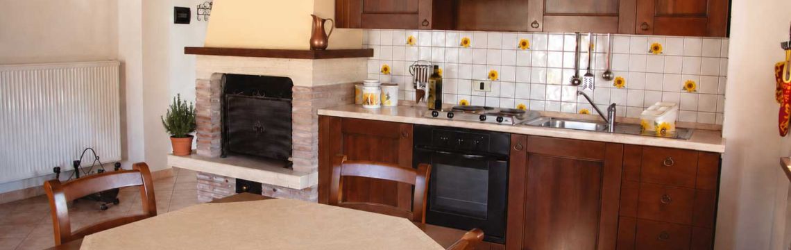 Cucina rustica umbra in agriturismo: camino, mobili in legno, piastrelle con girasoli, atmosfera accogliente per turisti.