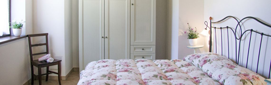 Camera accogliente con letto matrimoniale in un agriturismo umbro, decorata con biancheria floreale e arredi rustici.