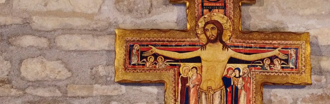 Crocifisso medievale in legno dorato incorniciato su parete di pietra, simbolo di spiritualità umbra nell'agriturismo.